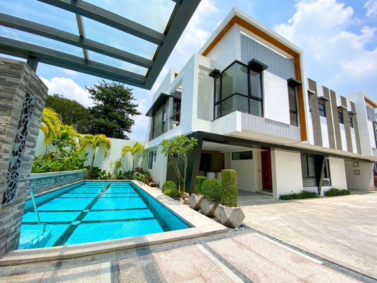 Luxurious and modern looking white townhouse with a rectangular swimming pool beside it